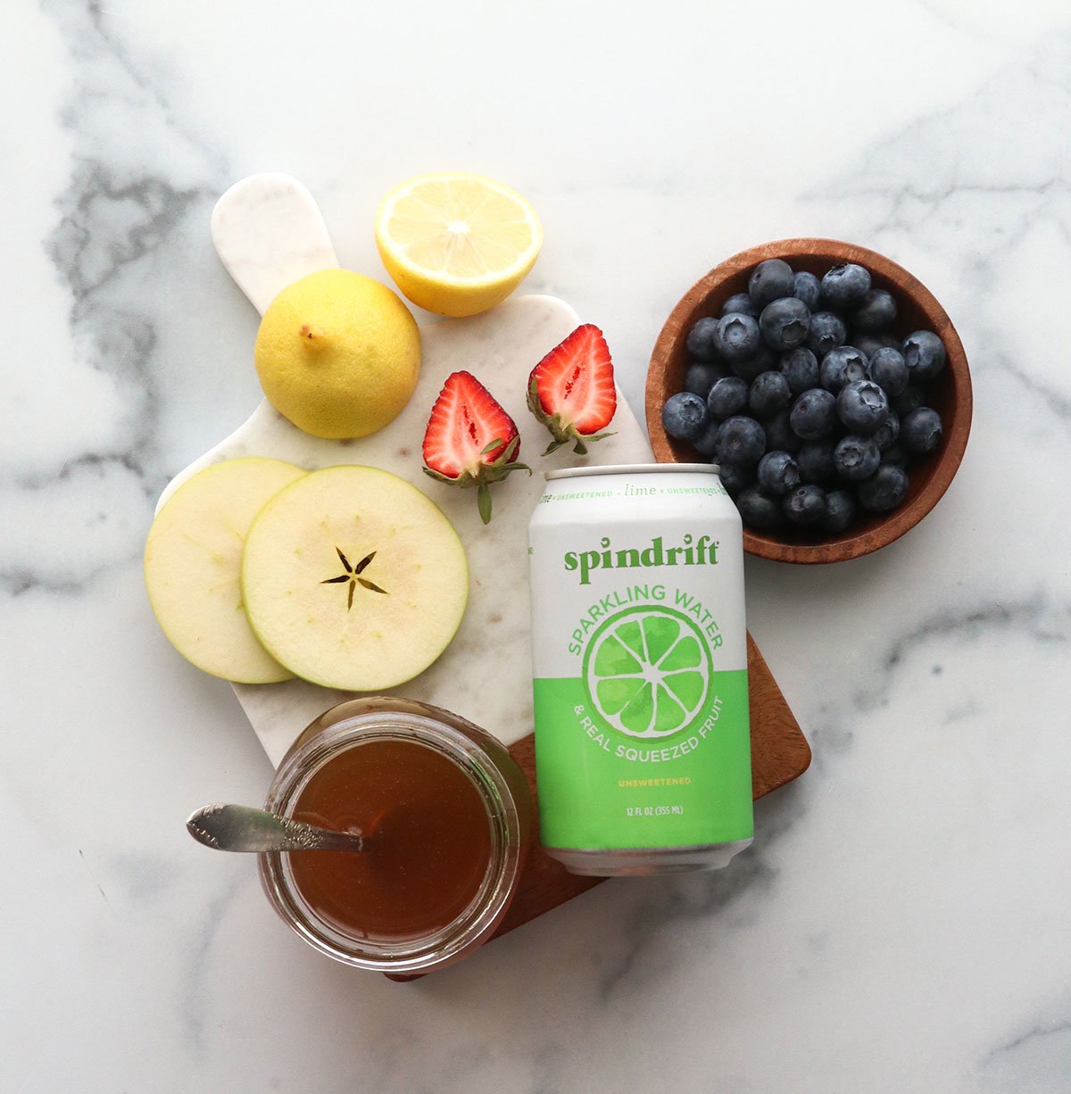 fresh fruit, simple syrup, and sparkling water laying on a marble surface.