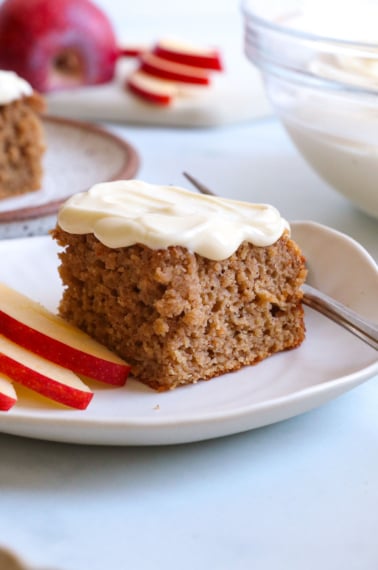 applesauce cake slice topped with cream cheese frosting on a white plate.