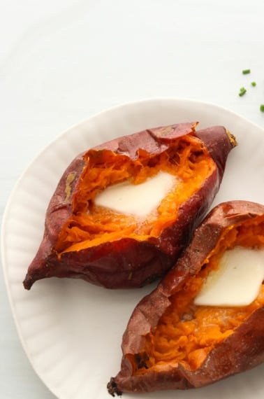 two baked sweet potatoes on a white plate topped with butter.