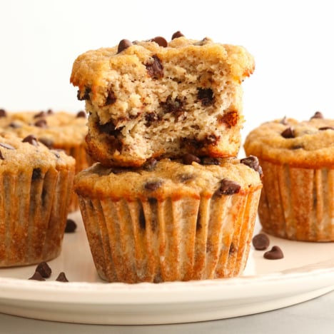 almond flour banana muffins stacked on a plate with bite taken out of it.