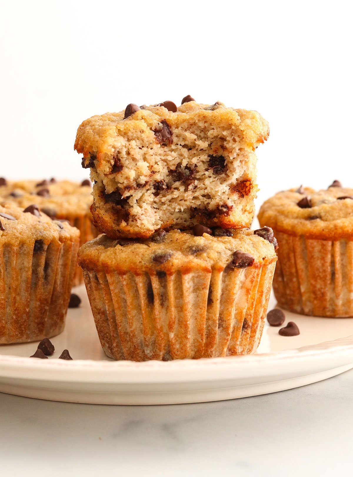 almond flour banana muffins stacked on a plate with bite taken out of it.