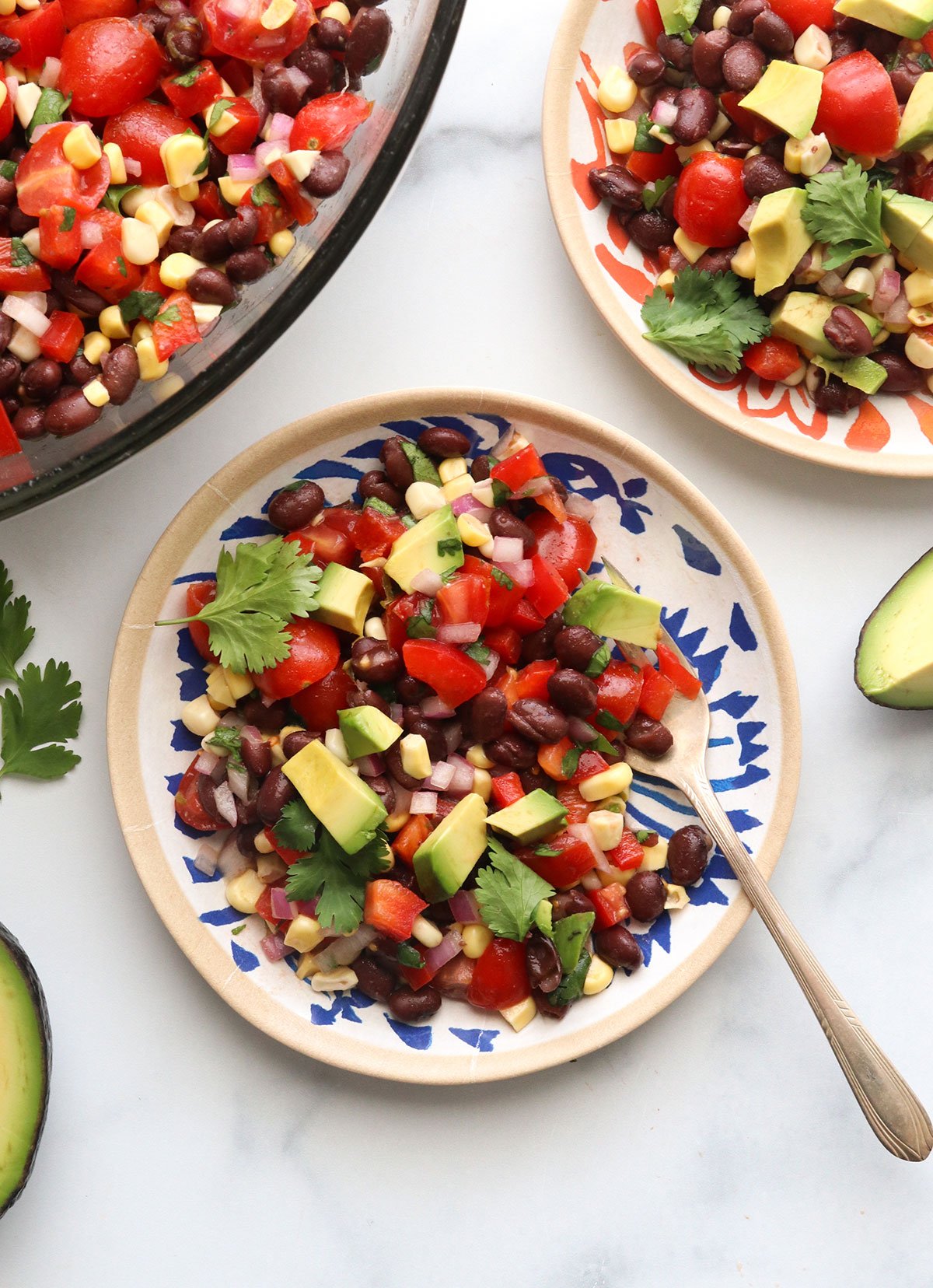 black bean salad served on two colorful plates and topped with avocado chunks.