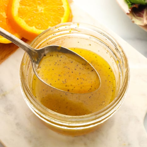 orange dressing lifted up on a spoon over a glass jar.