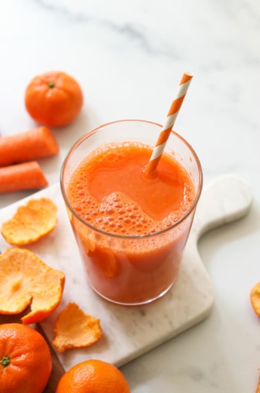 Carrot juice served with a striped straw on a white marble board.