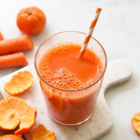 Carrot juice served with a striped straw on a white marble board.