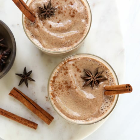 two glasses of chai smoothies with cinnamon sticks inside.