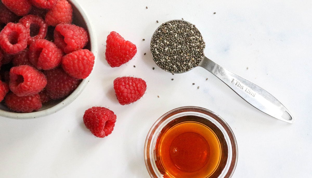 chia seeds raspberries and maple syrup on white surface