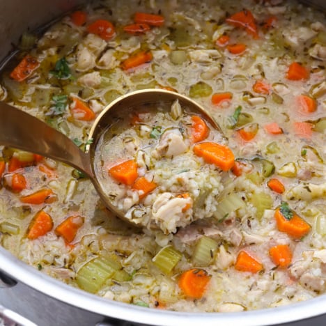 Chicken and rice soup scooped on a gold ladle in a pot.