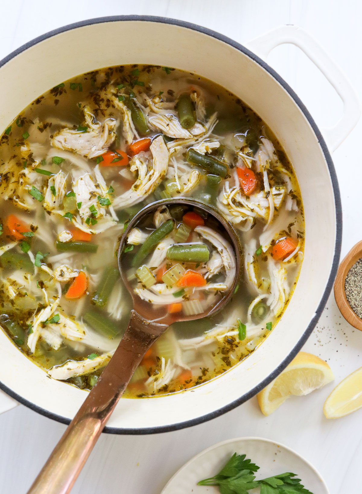 chicken vegetable soup in white pot with ladle.