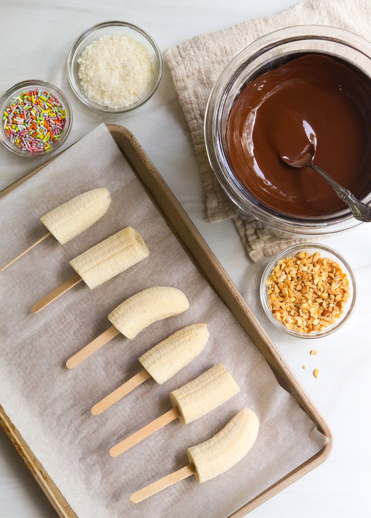 sliced bananas near a bowl of melted chocolate and toppings.