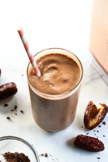 Chocolate date smoothie with a pink straw and dates around it.