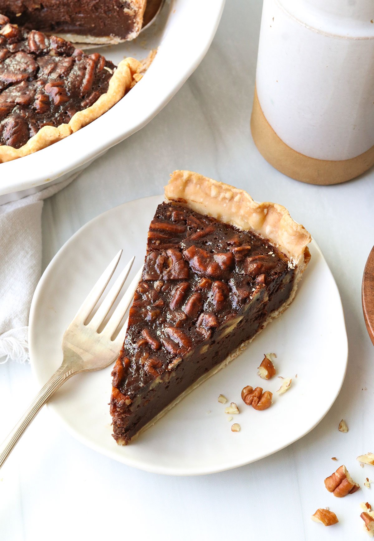 Chocolate pecan pie slice served on a white plate.