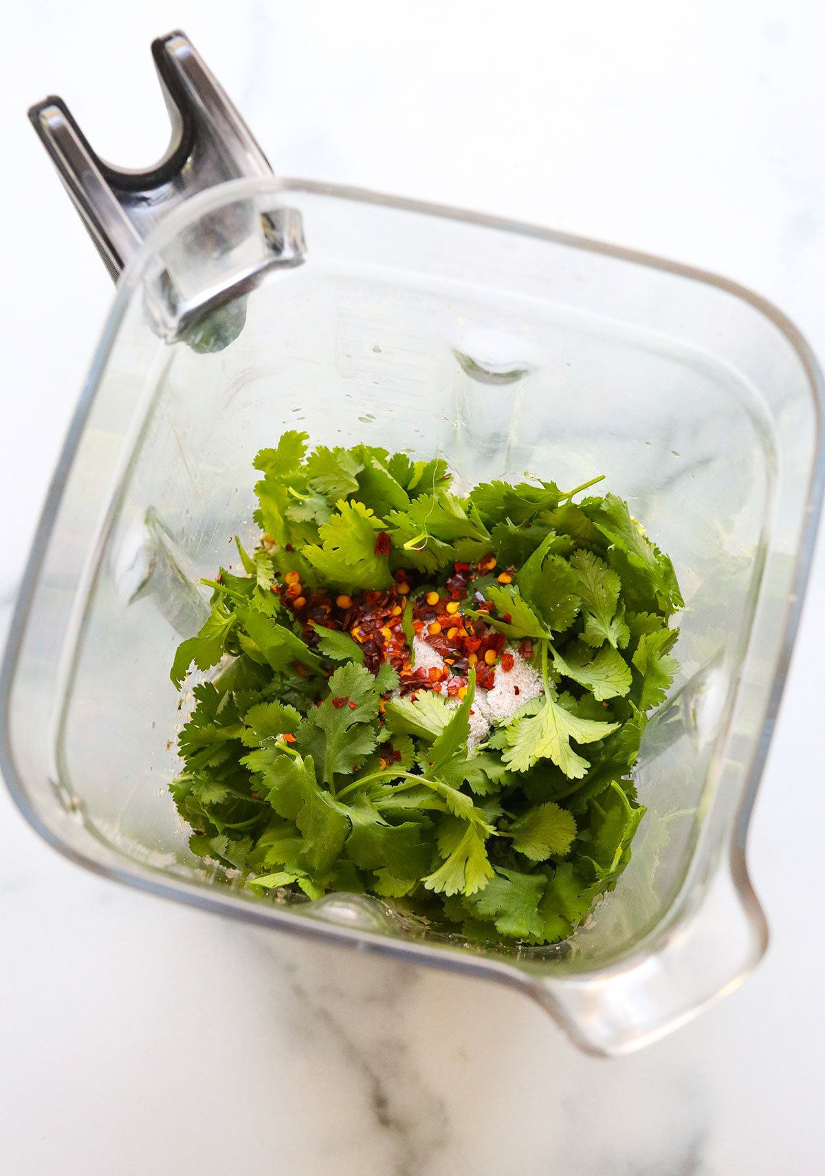 cilantro and red pepper flakes added to a blender.