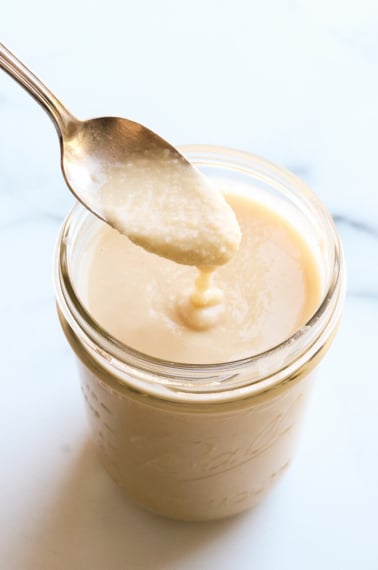 homemade coconut butter dripping off of a spoon into a jar.