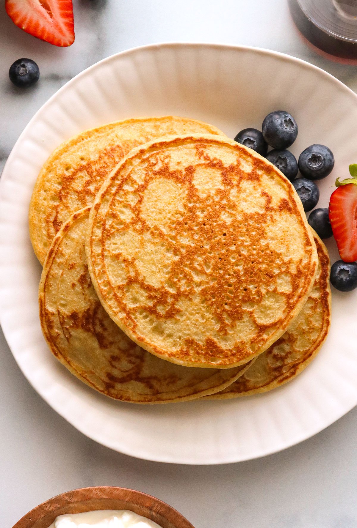 cottage cheese pancakes stacked on a white plate with berries.