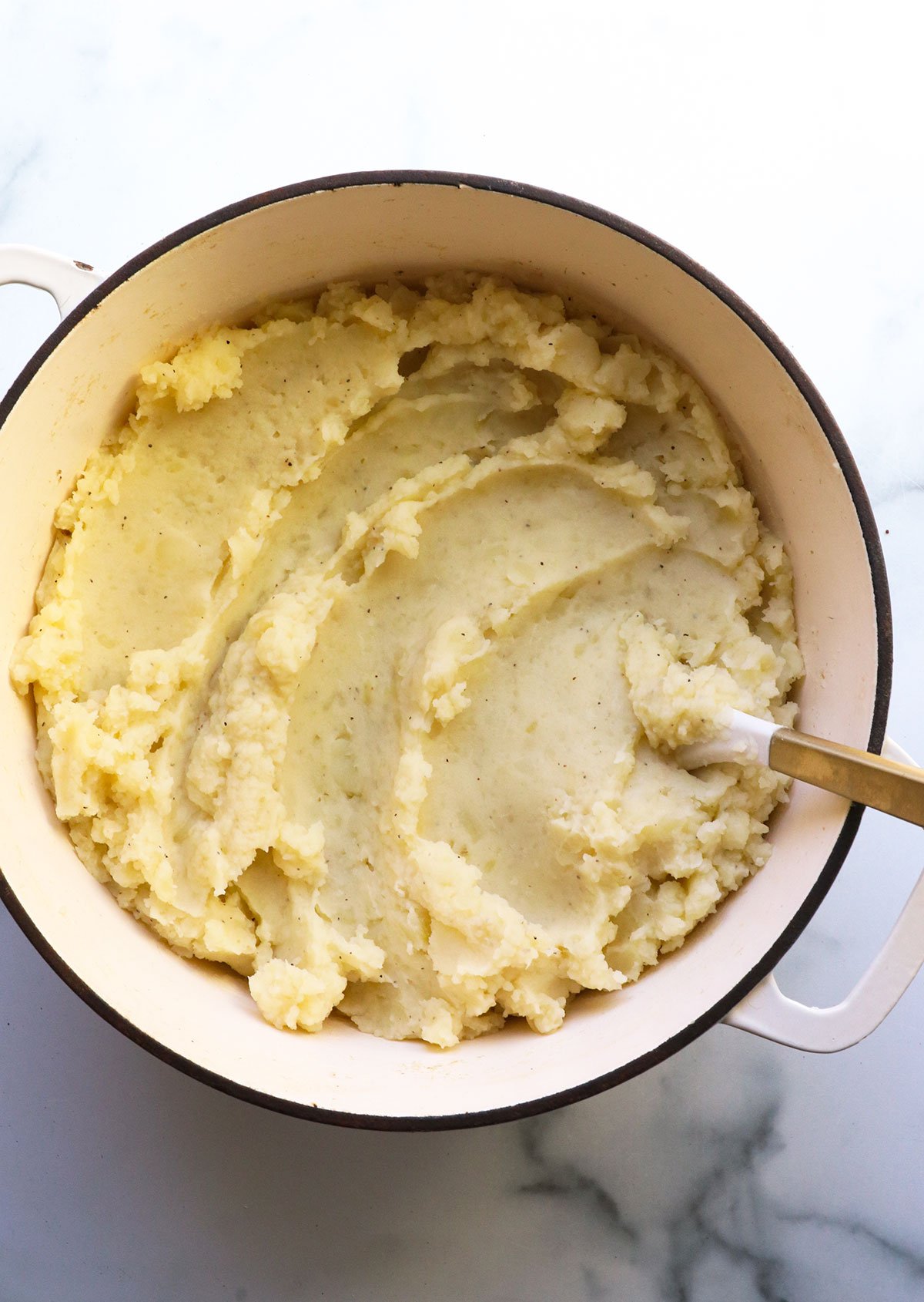 mashed potatoes in a white pot with a wooden spoon.