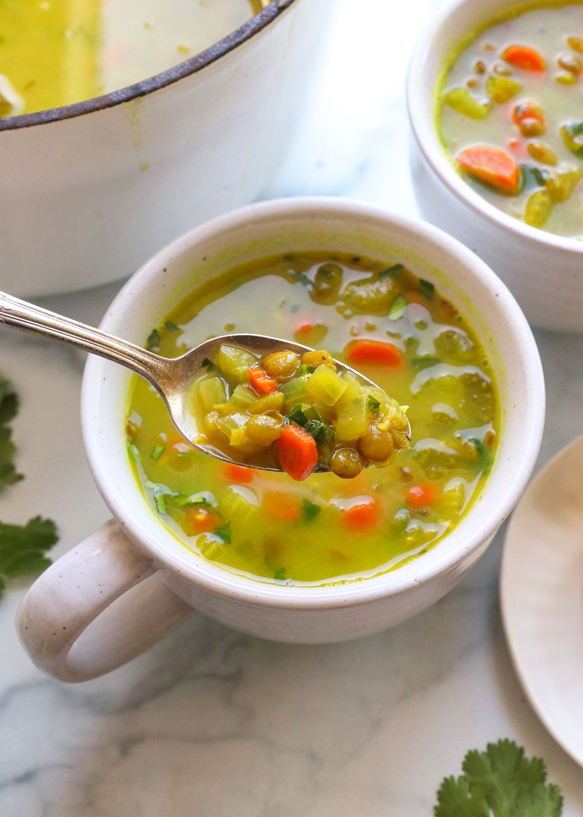 spoon lifting up some detox soup from a white mug with lentils and carrots.