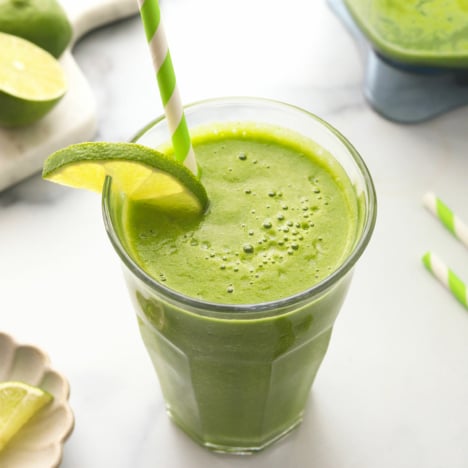 detox smoothie served in a glass with a lime slice and green paper straw.