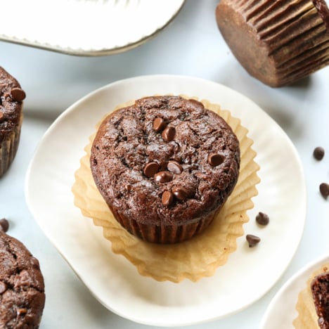 Chocolate zucchini muffin served on a white plate with the wrapper peeled off.