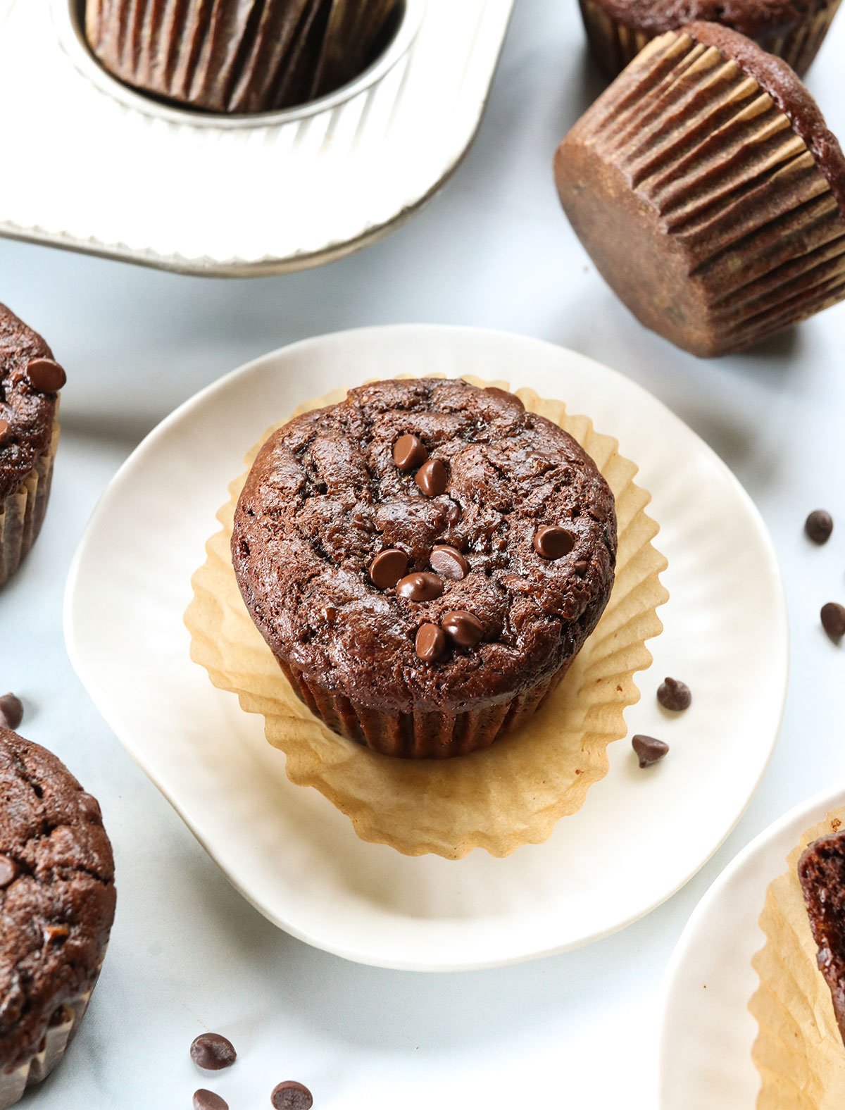 Chocolate zucchini muffin served on a white plate with the wrapper peeled off.