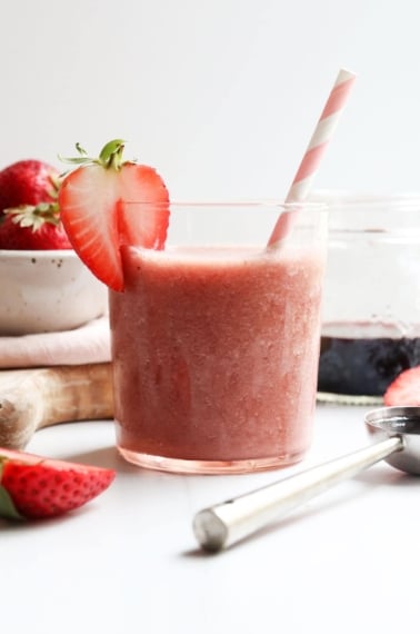 elderberry smoothie in glass with pink straw and strawberry