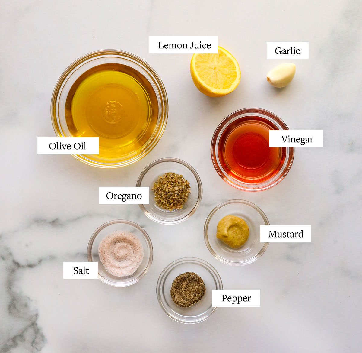 Greek dressing ingredients labeled on a marble surface.