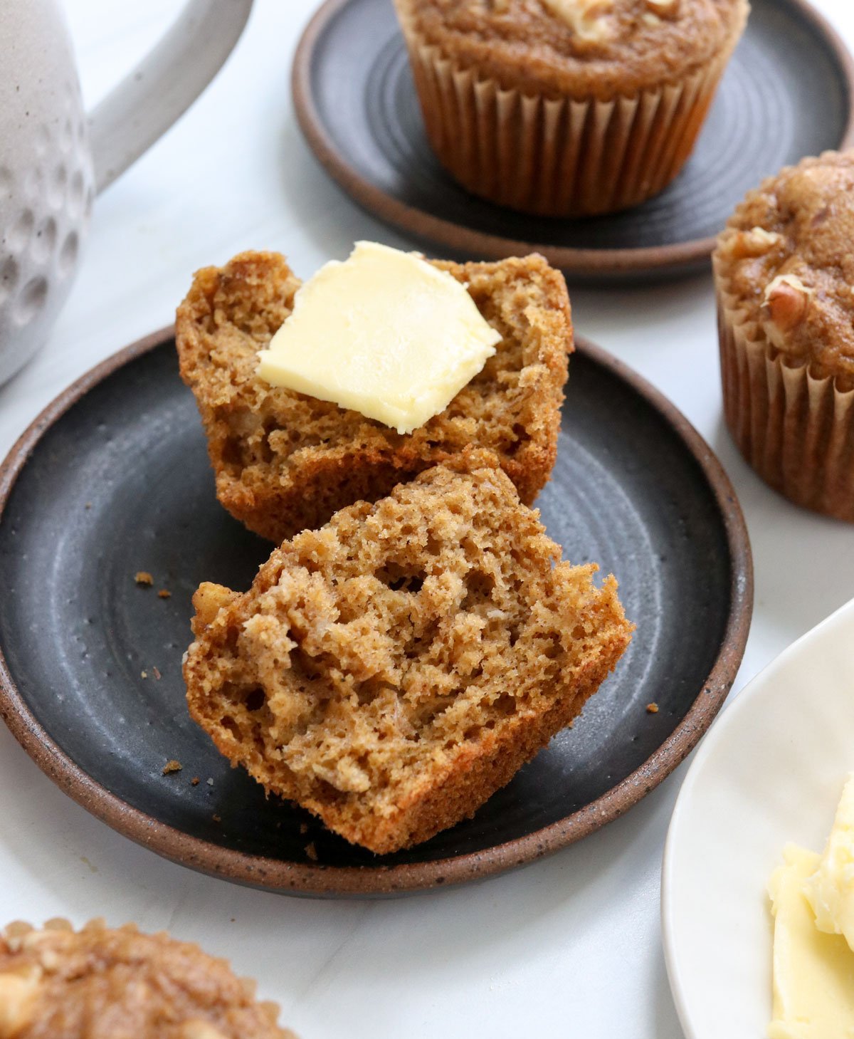 healthy banana muffin split in half on black plate.