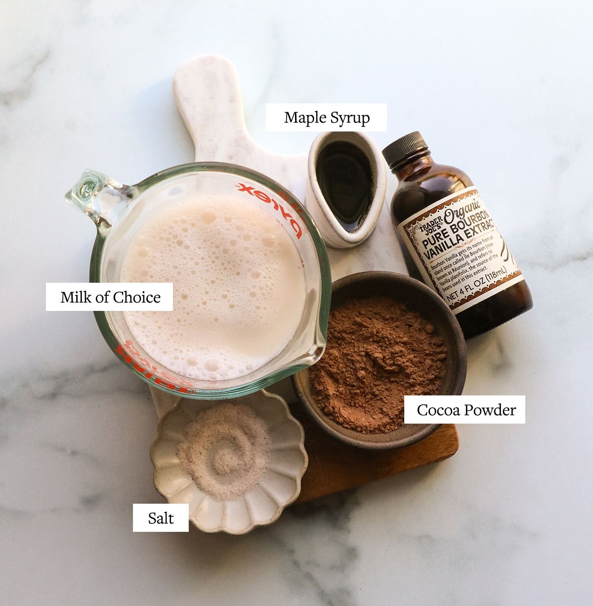 milk, cocoa powder, vanilla extract, maple syrup, and salt resting on a white board. 