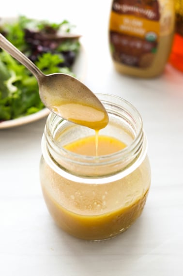 honey dijon vinaigrette dripping off a spoon into a jar.