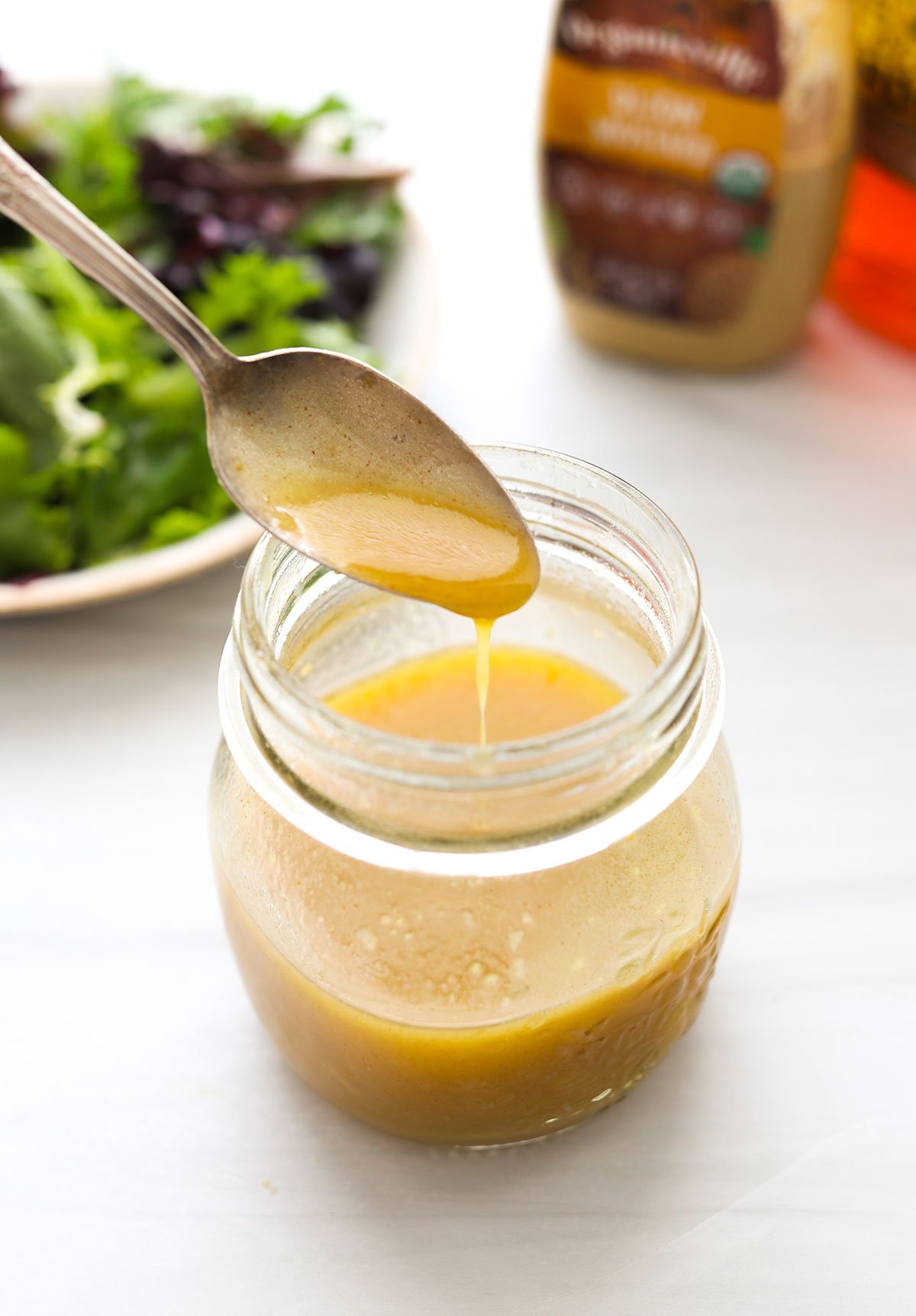 honey dijon vinaigrette dripping off a spoon into a jar.