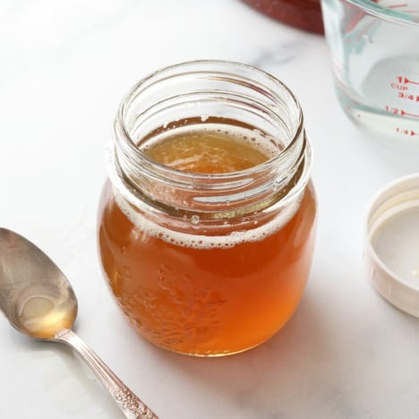 honey simple syrup in a glass jar near a spoon.