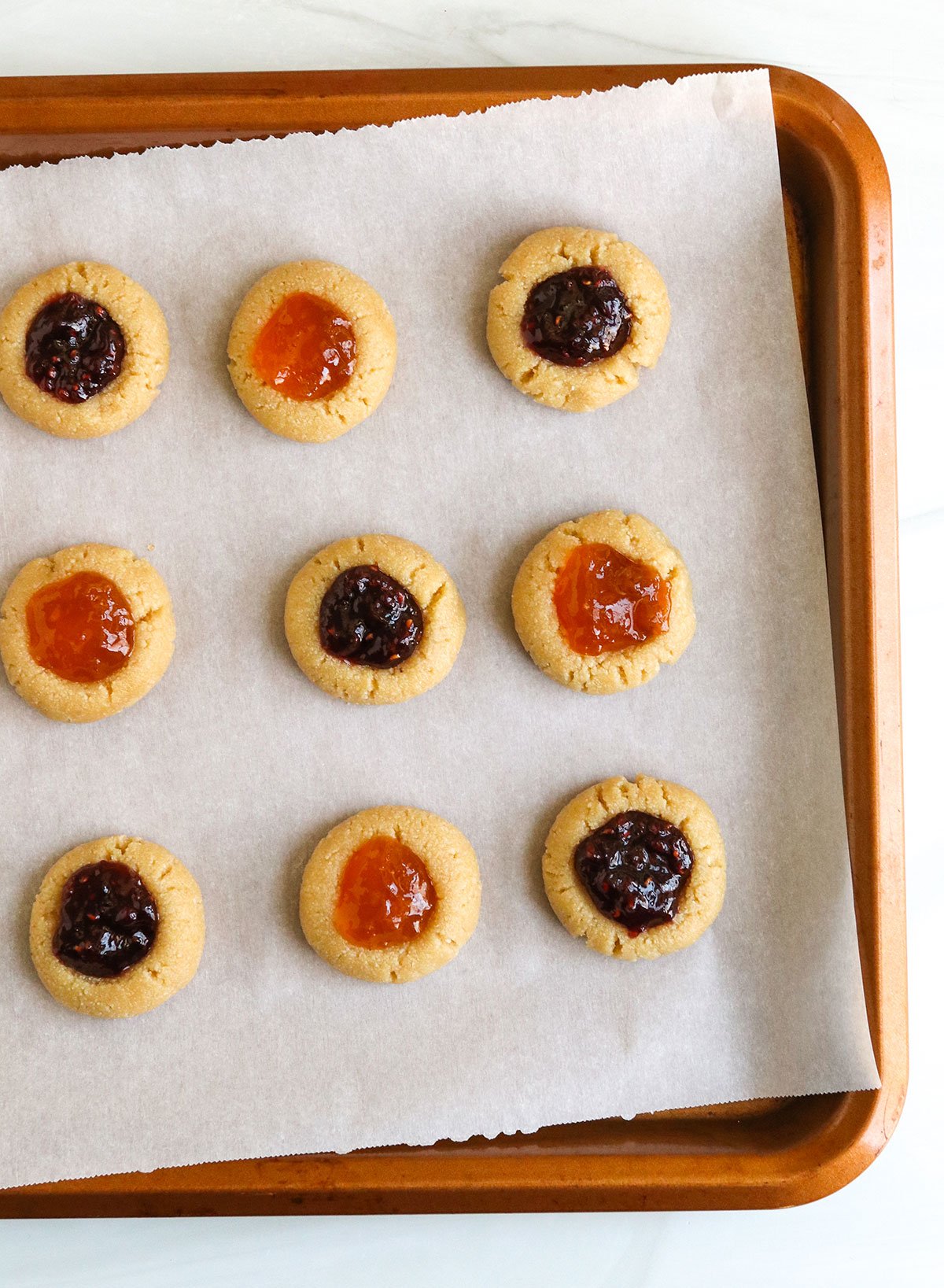 jam added to thumbprint cookies on baking sheet.