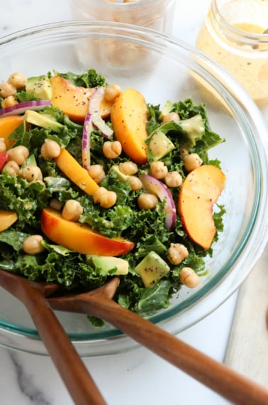 kale and peach salad with serving tongs