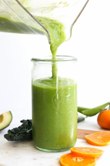 kale smoothie poured into a glass from the blender pitcher.