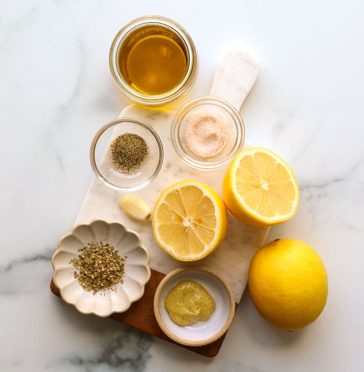 sliced lemons, olive oil, salt, pepper, oregano, and mustard on a white board.