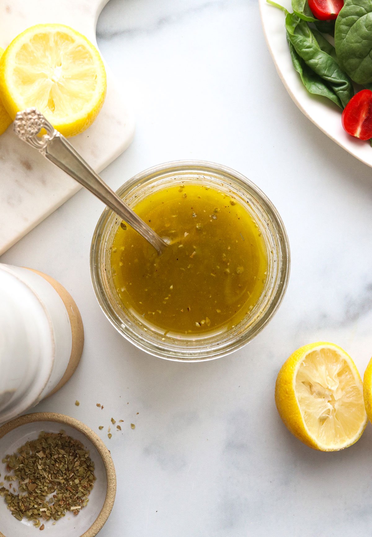 lemon dressing stirred together with a spoon next to a plate of salad.