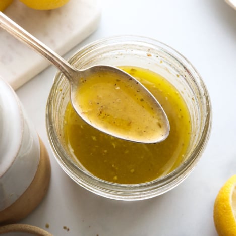 spoon lifted up with lemon vinaigrette over a jar.