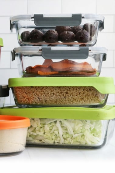 meal prep containers filled with ingredients stacked on white counter.