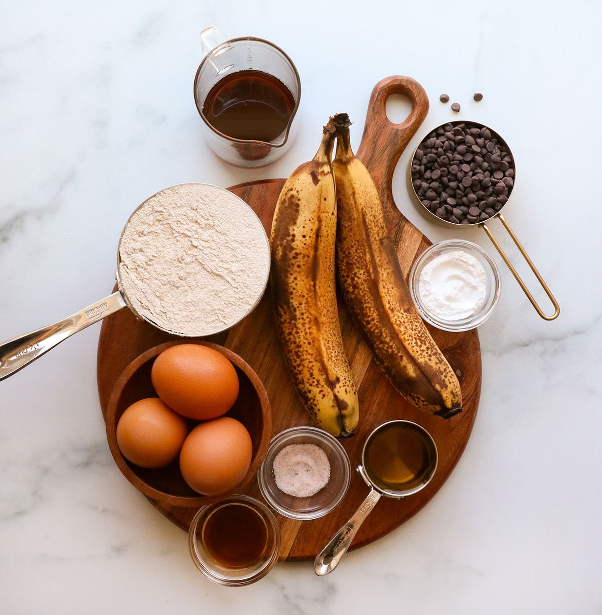 ripe bananas, oat flour, eggs, and mini chocolate chips arranged on a cutting board.