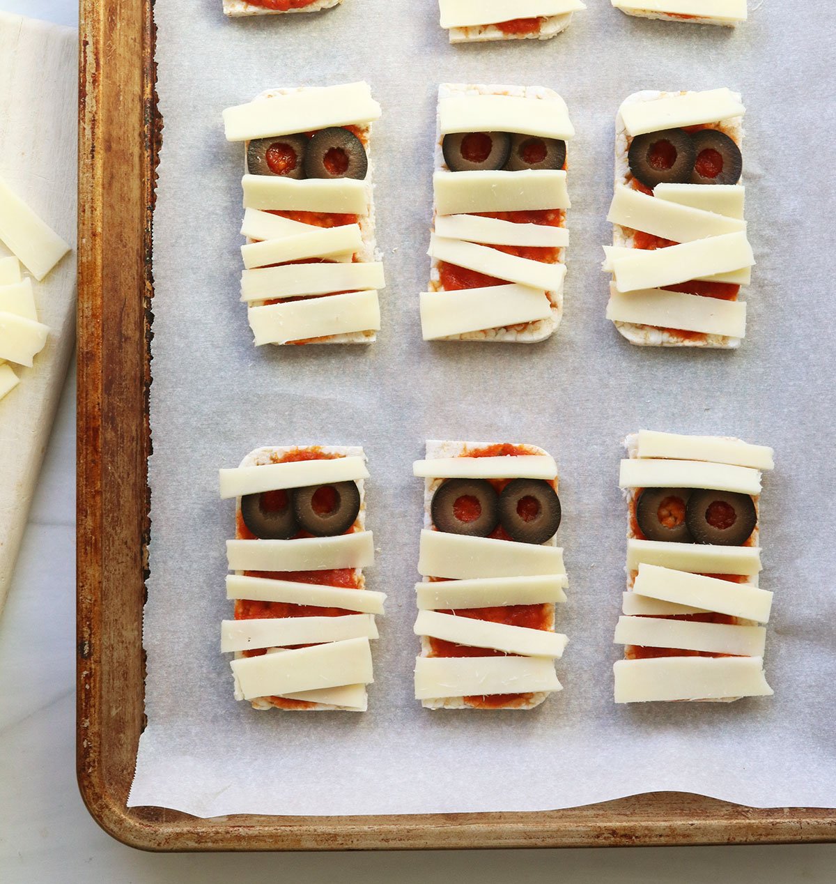 mini pizzas topped with slices of cheese and olives to look like mummys.