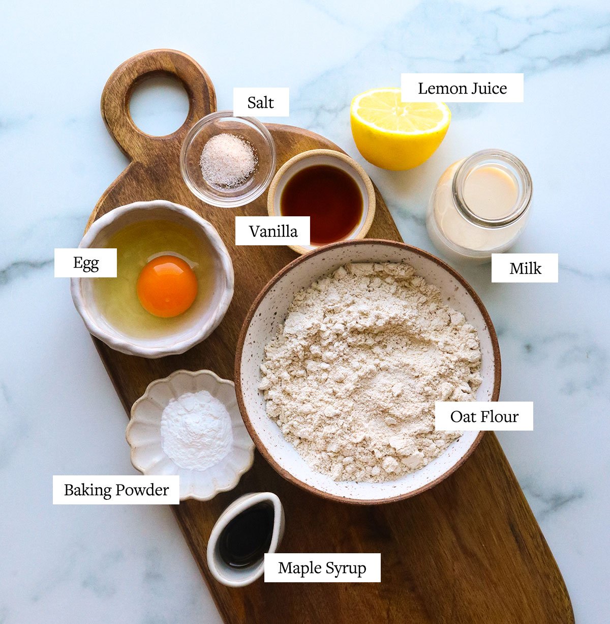 oat flour pancake ingredients labeled on a cutting board and marble surface.