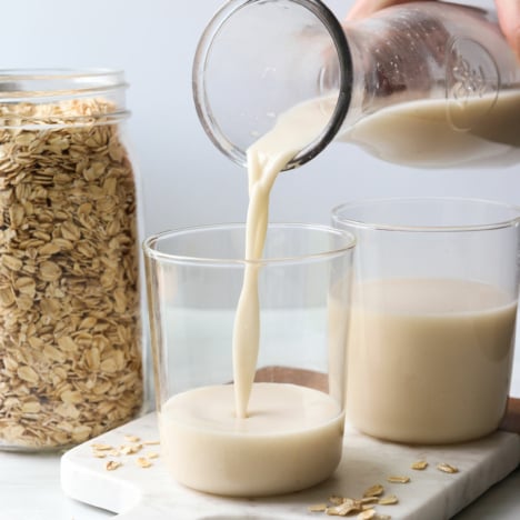 homemade oat milk poured into a glass on a marble cutting board.