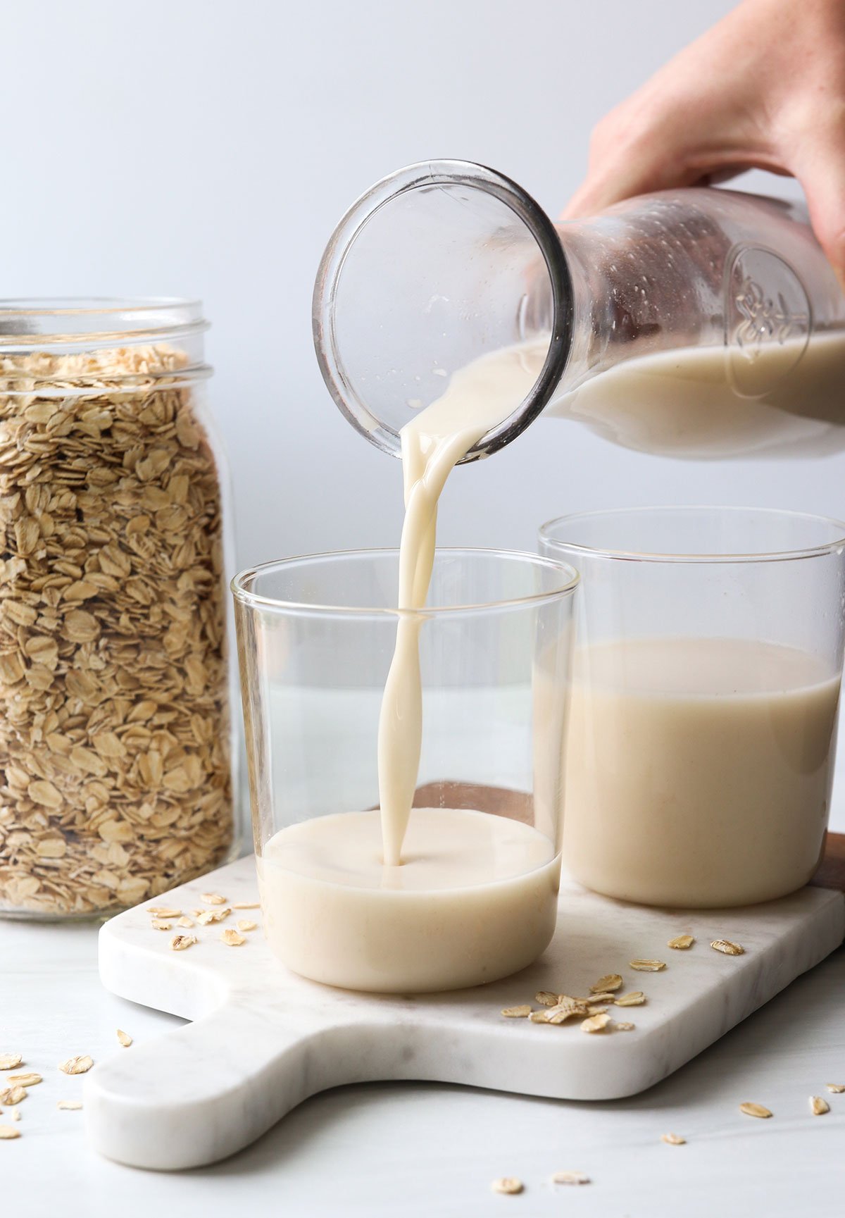 homemade oat milk poured into a glass on a marble cutting board.