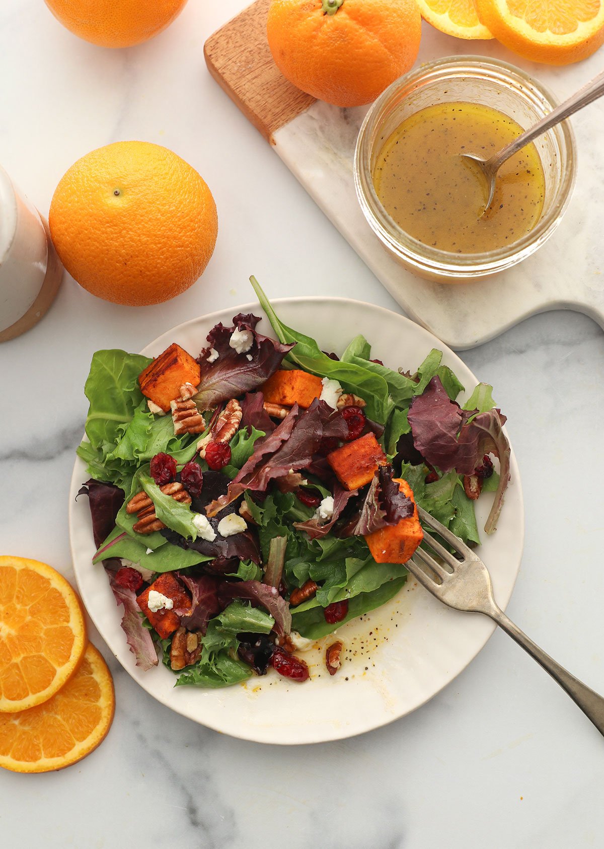 orange vinaigrette served on a salad plate with greens, sweet potatoes, pecans, and cranberries.