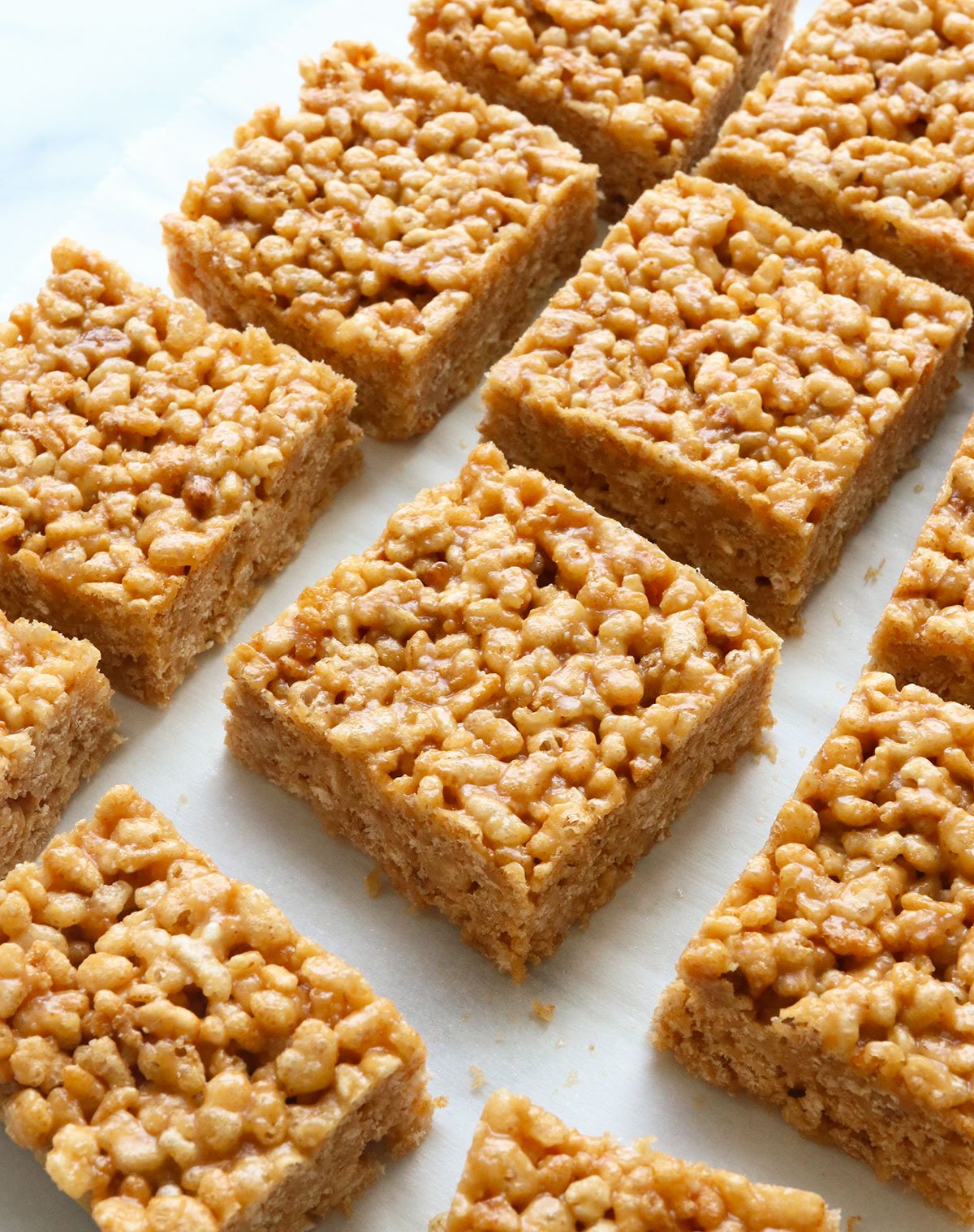 peanut butter rice crispy treats cut into squares on white parchment.