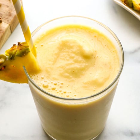 slushy pineapple smoothie in a glass with a yellow straw.