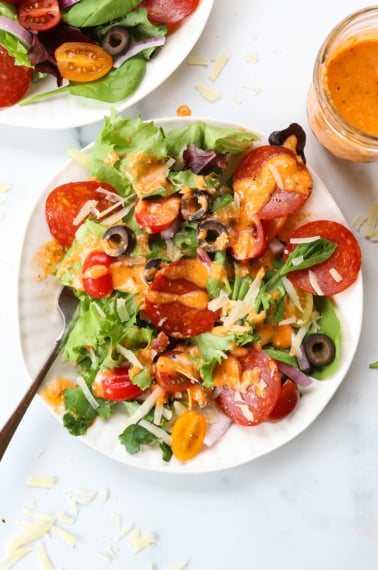 pizza toppings added to a plate of greens and drizzled with the dressing.