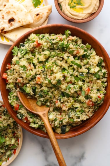 quinoa tabbouleh served in a wooden bowl with a wooden spoon.