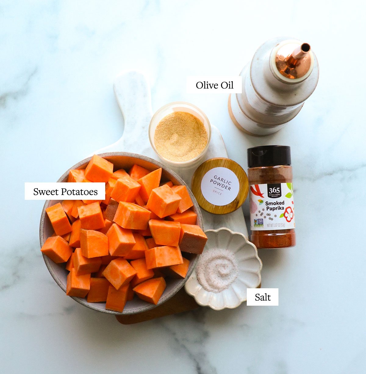 sweet potato cubes near a jar of garlic powder, smoked paprika, olive oil, and salt.