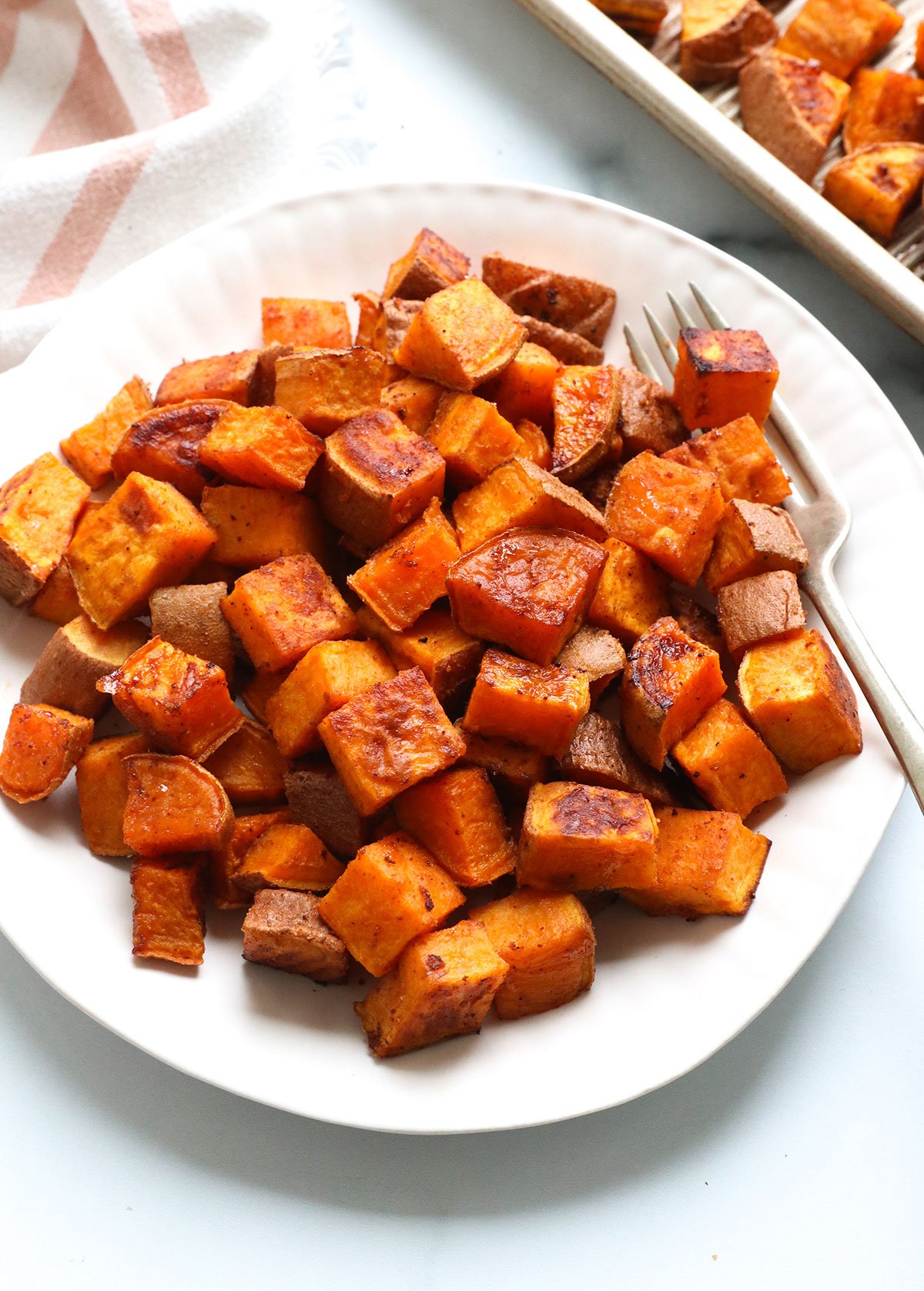 roasted sweet potato cubes served on a white plate with a fork.